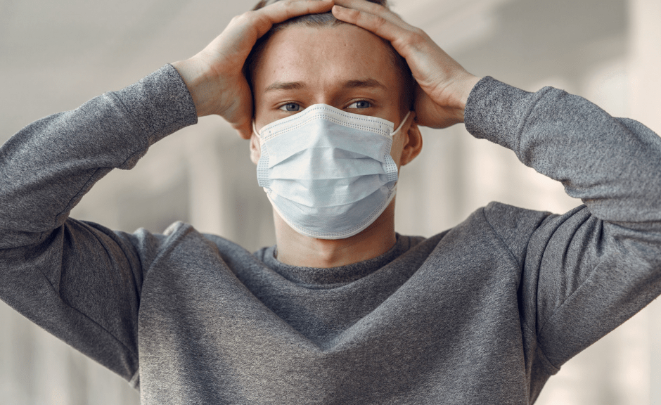 Image of person in mask holding their head--illustrating stress