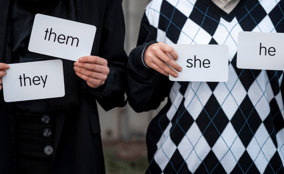 an image of two people holding placards with pronouns on them to introduce a piece about anti-transgender rhetoric