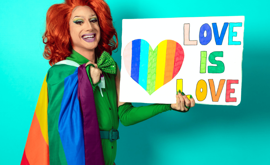 A picture of a drag queen holding a "love is love" sign to introduce an article discussing the unhealthy rhetoric of anti-drag legislation