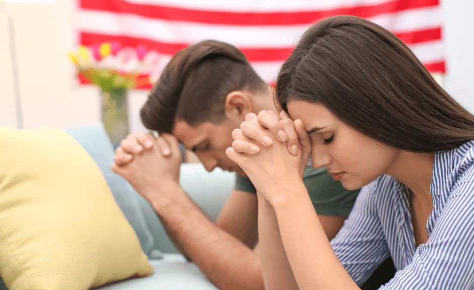 Photo of two white young people praying in front of a flag to introduce an article against Christian nationalism